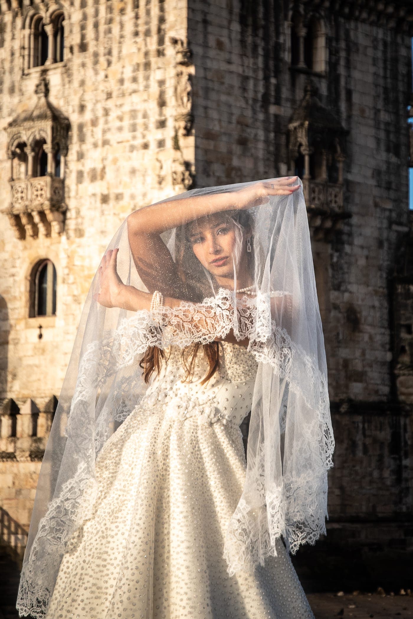 Ball gown and veil raised against the Torre de Belém at sunrise