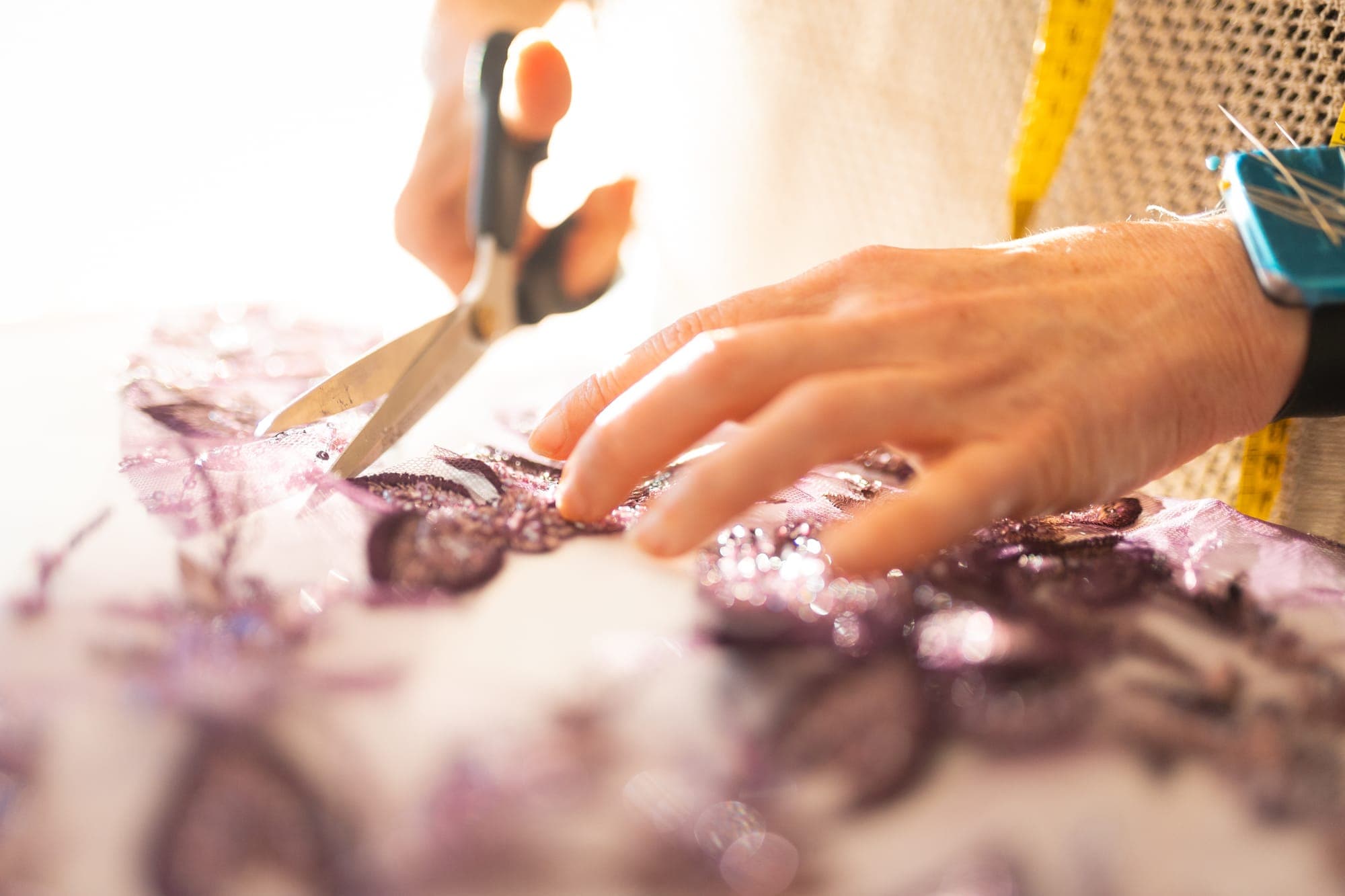 Close-up of hands cutting individual aubergine lace appliqué motifs from fabric with small scissors