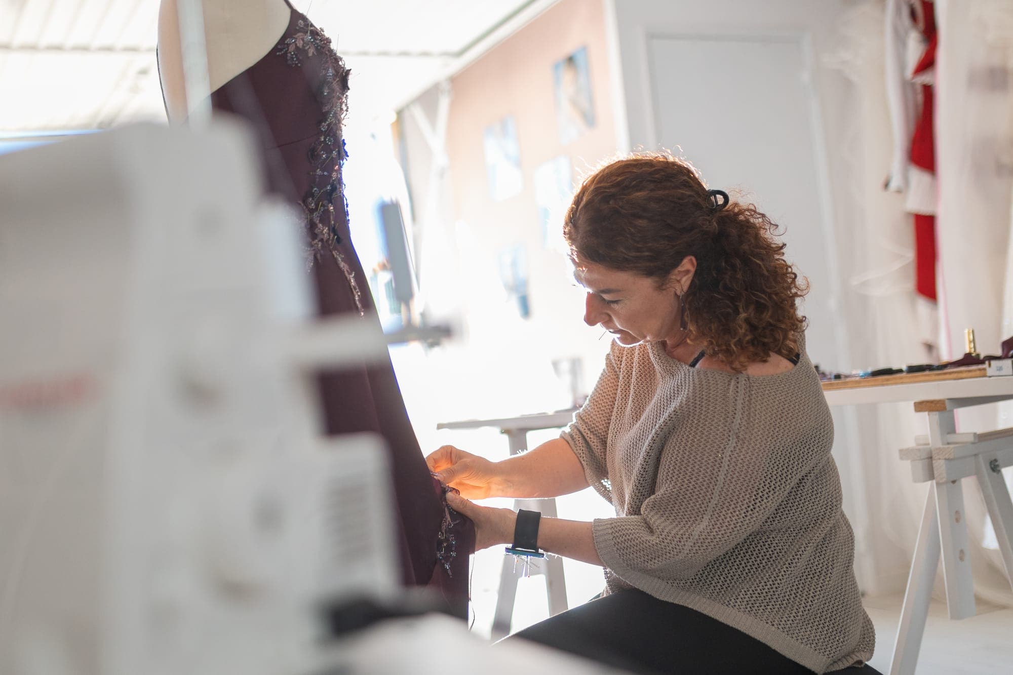Designer hand-finishing an aubergine evening gown with floral lace appliqué at her workstation