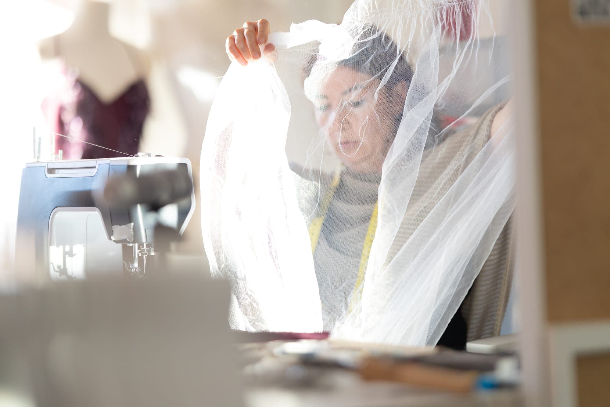 Seamstress holding a length of bridal tulle up against a bright window to inspect it