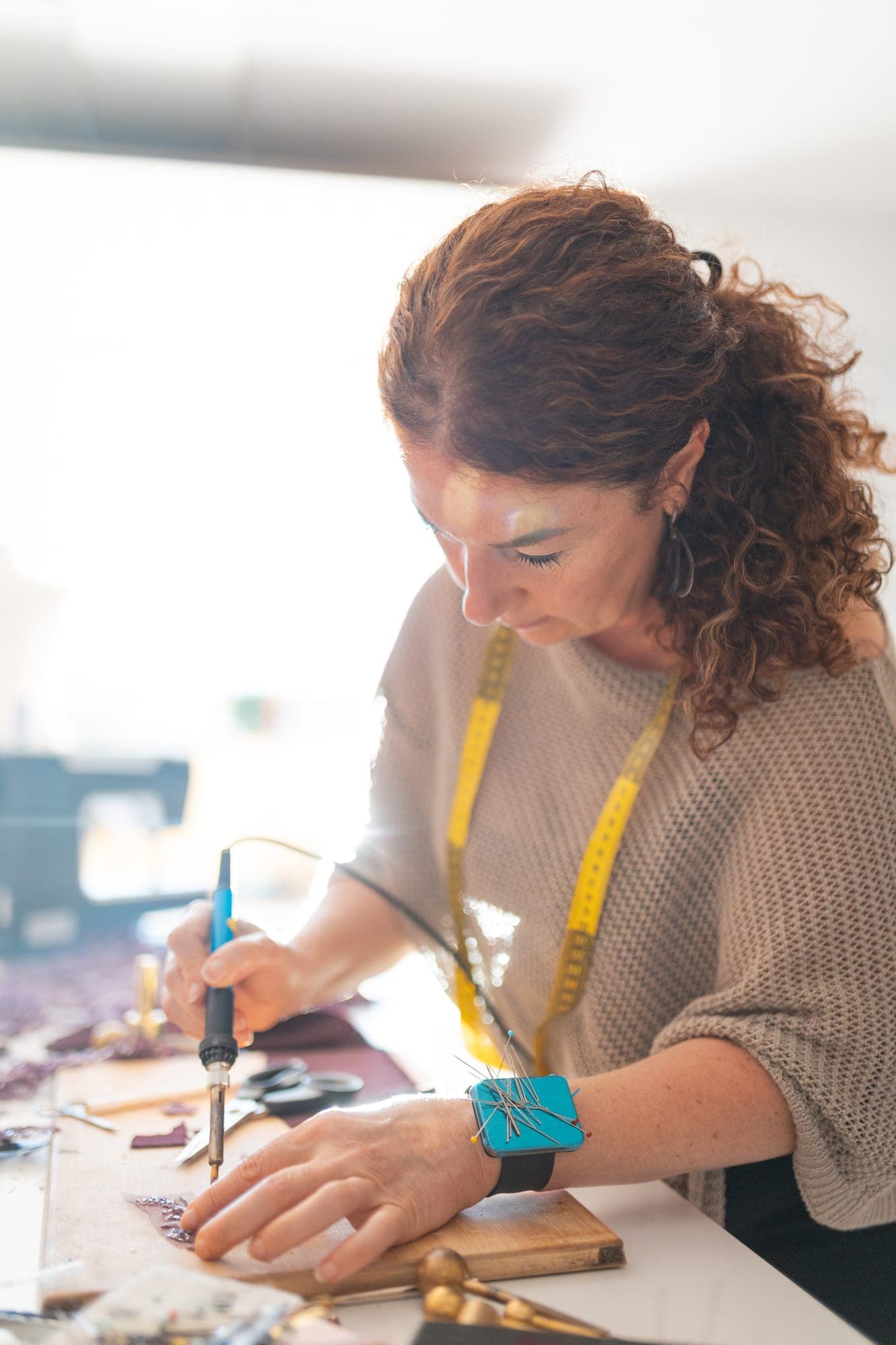 Craftswoman using a small heated tool to seal and shape the cut edge of a fabric petal