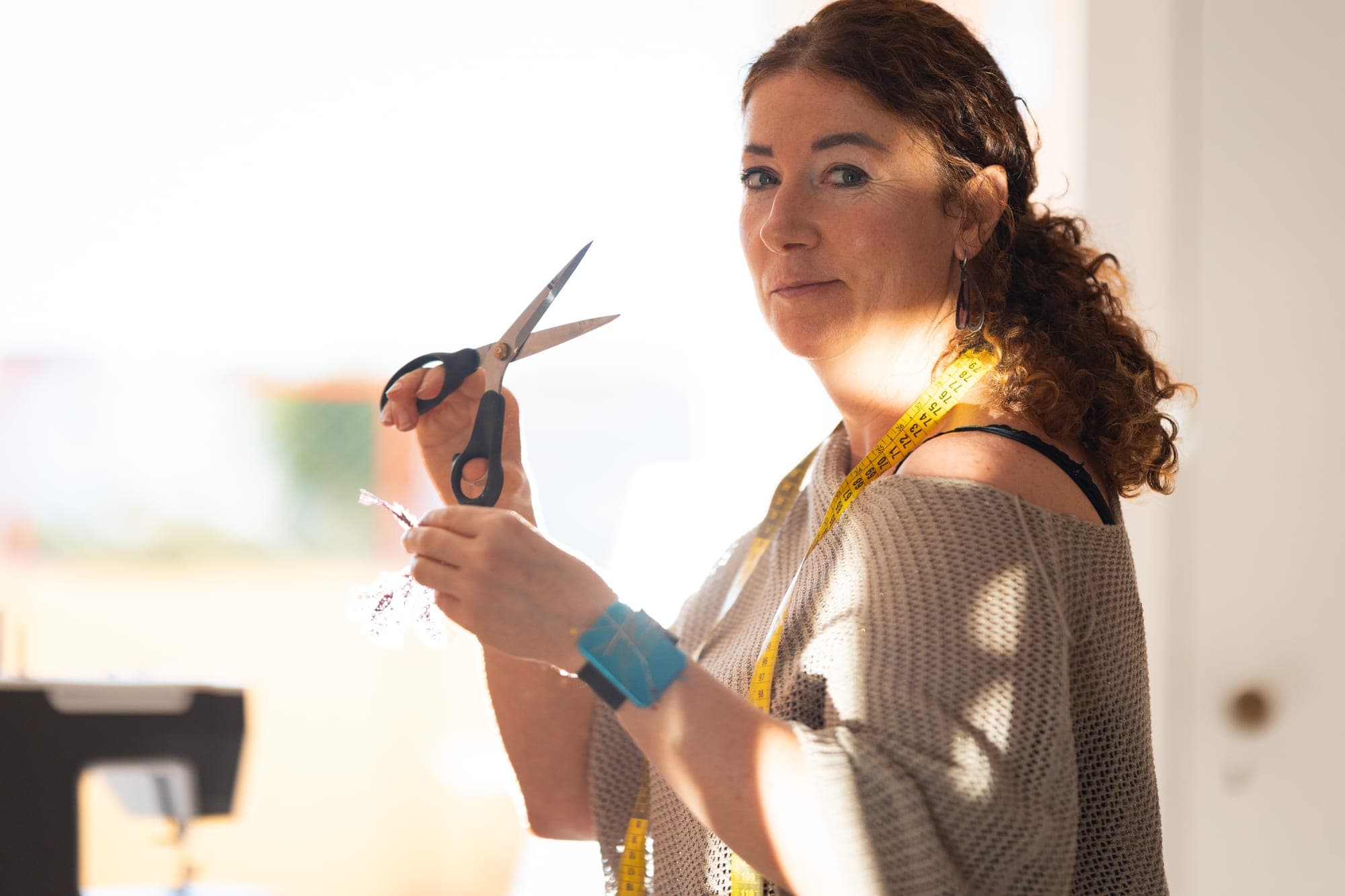 Portrait of a craftswoman holding open tailor's shears, a yellow measuring tape draped around her neck