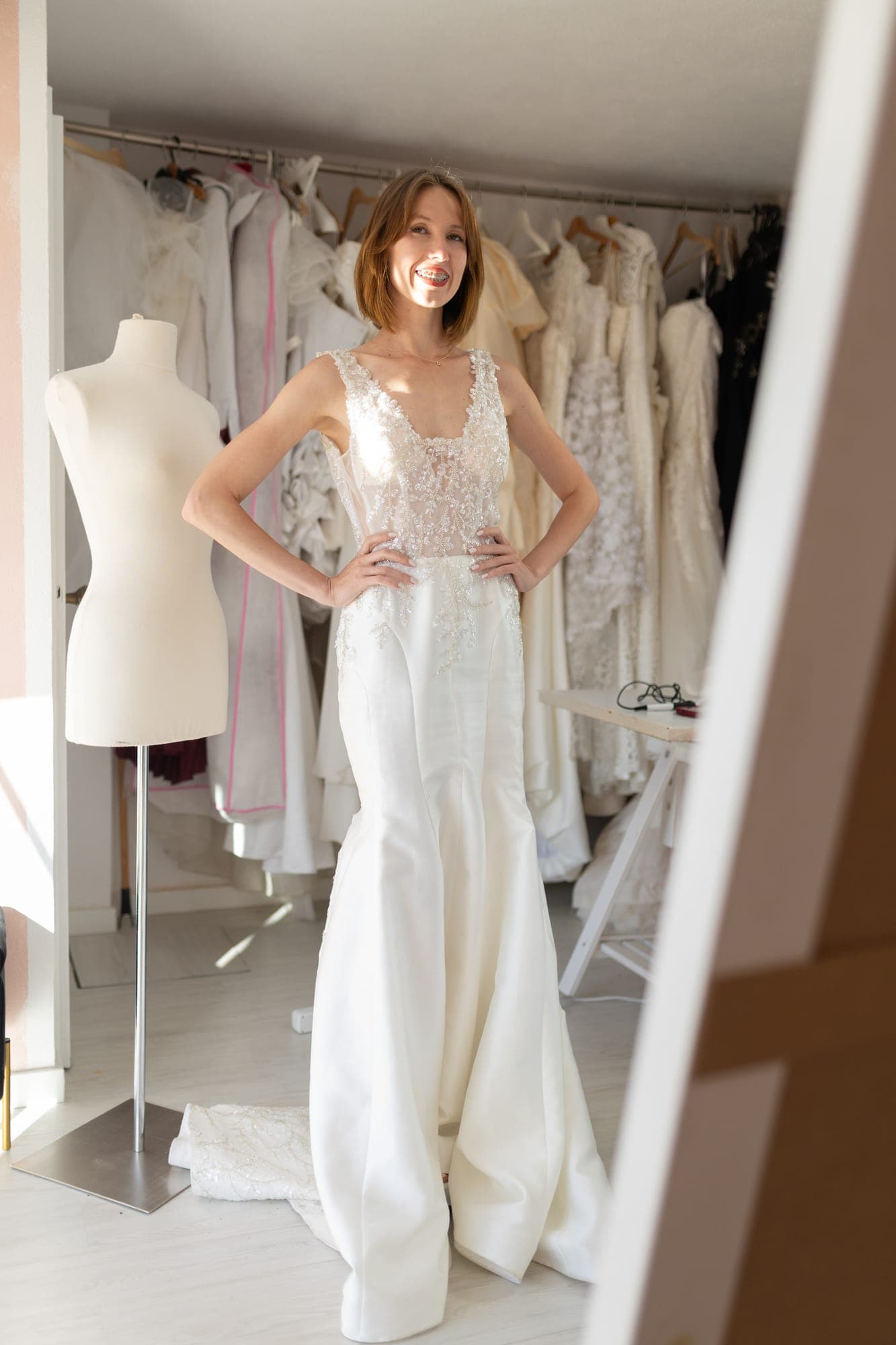 Model in an embroidered fishtail wedding gown standing beside the dress form used to build it