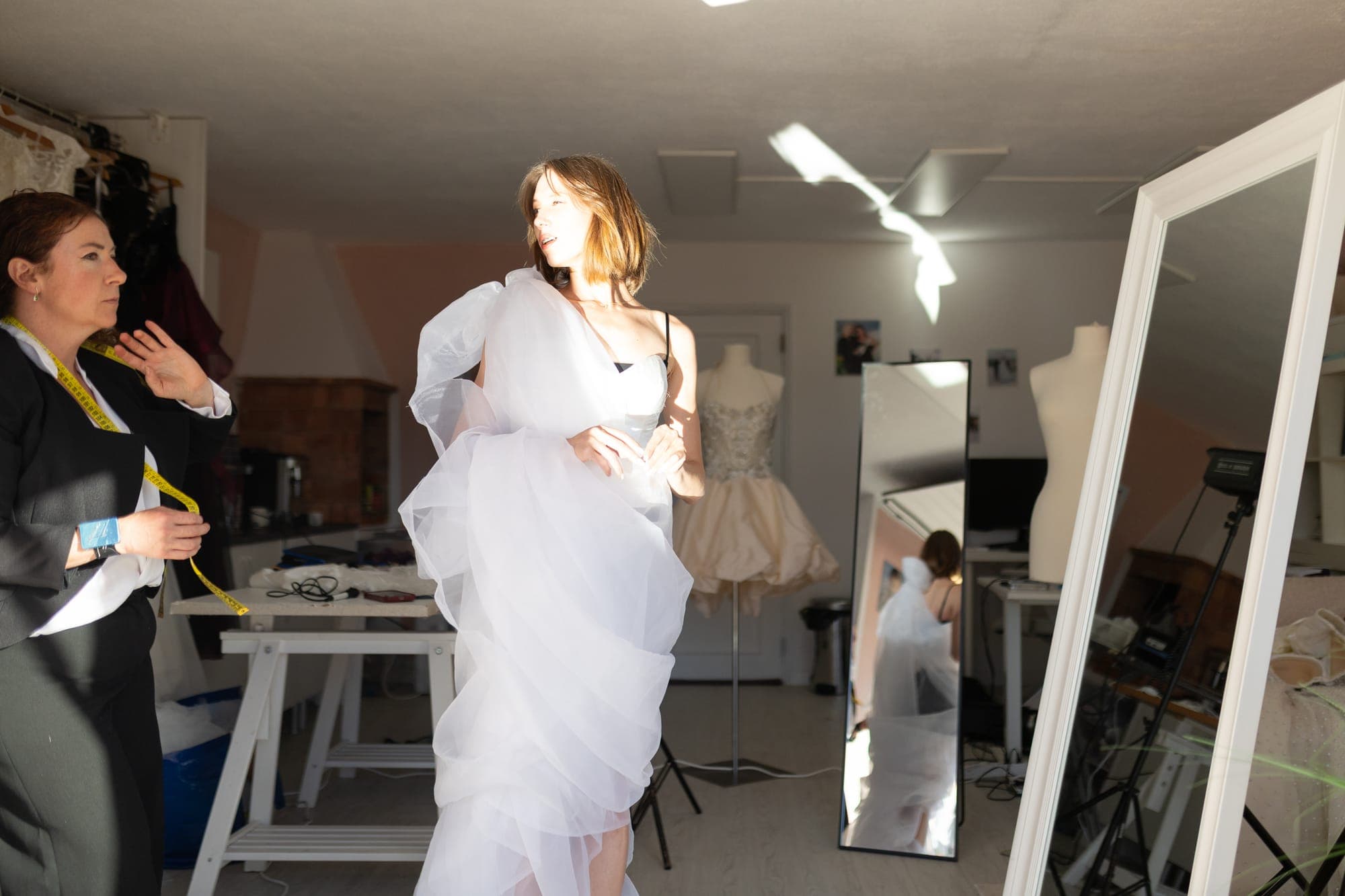 Model wearing a white ruffled tulle wedding gown mid-movement in the atelier, mirrors and dress forms behind her
