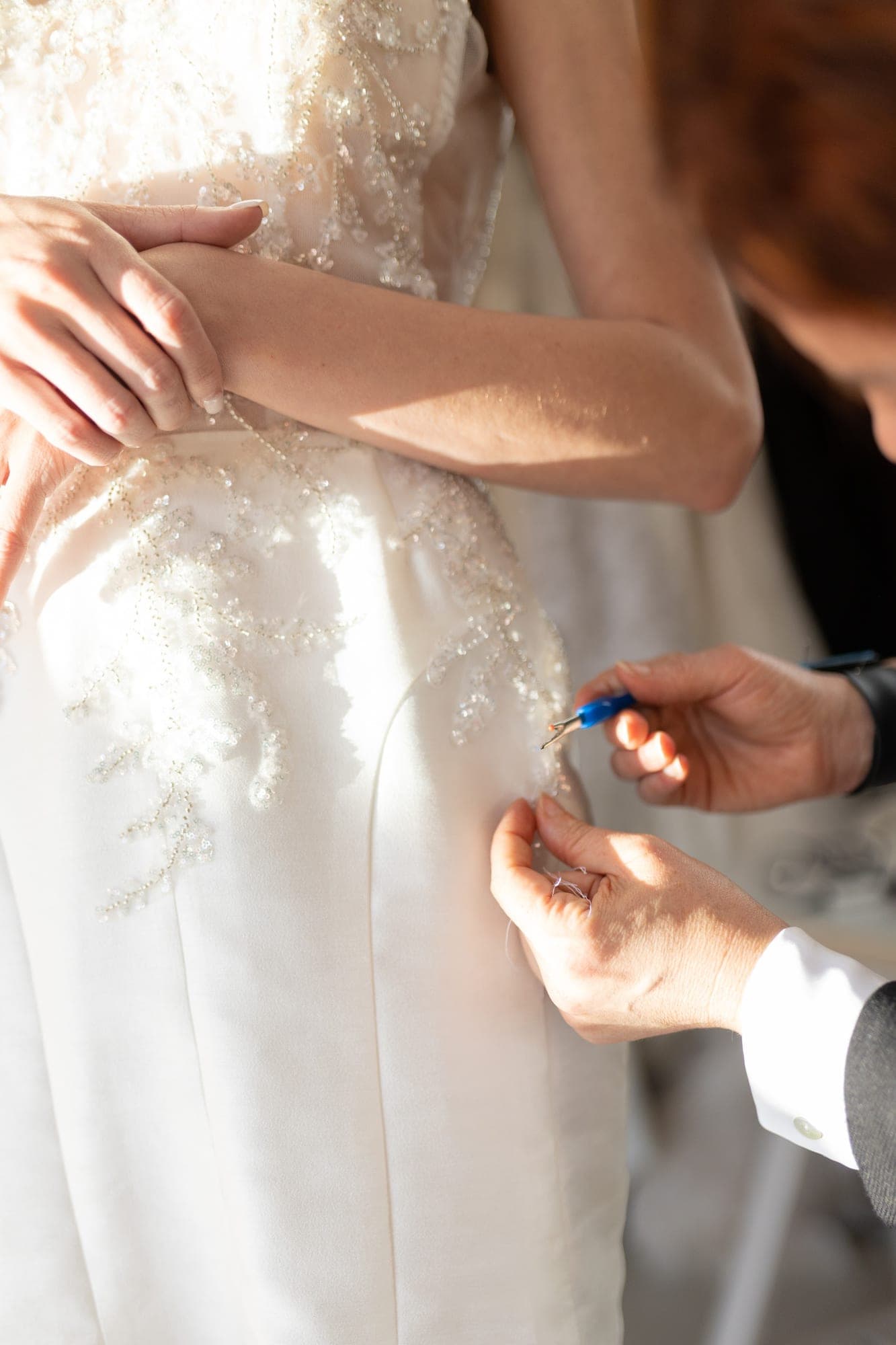 Hands adjusting the shoulder of a satin bridal gown during a fitting