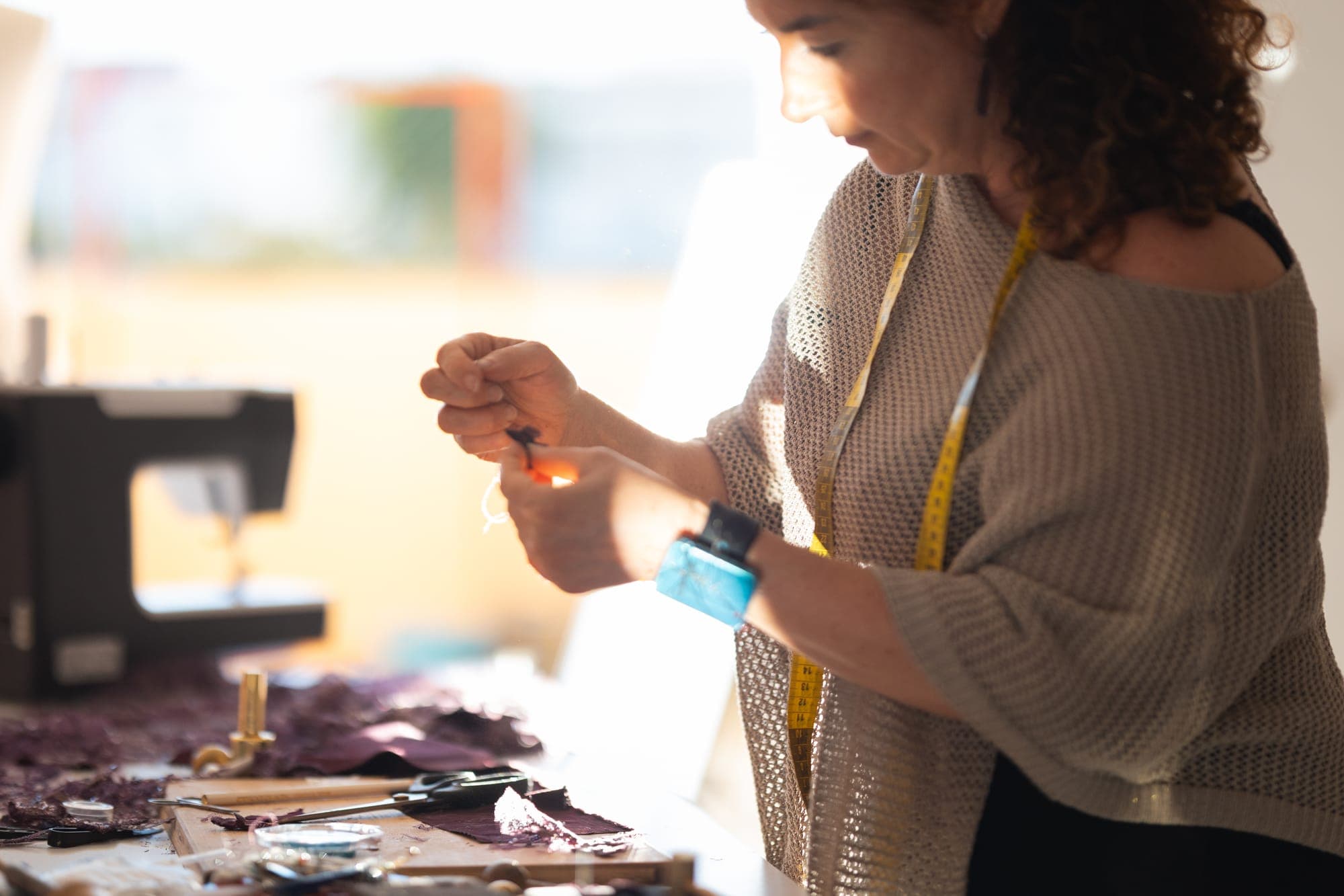 Hands placing a small shaped fabric petal onto a garment at a workbench scattered with cut lace