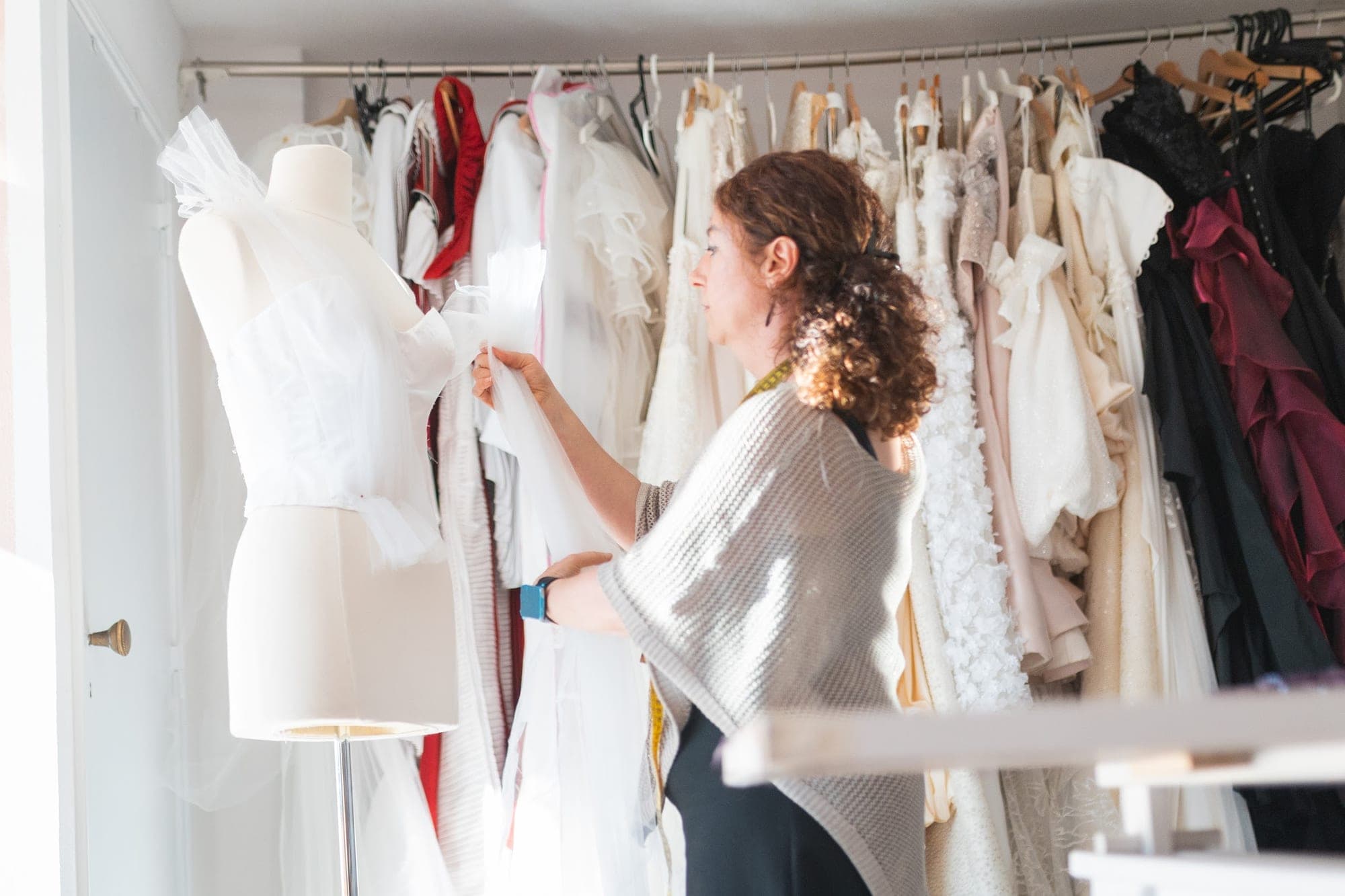 Rail of white bridal gowns and dress stands in a bright atelier workroom